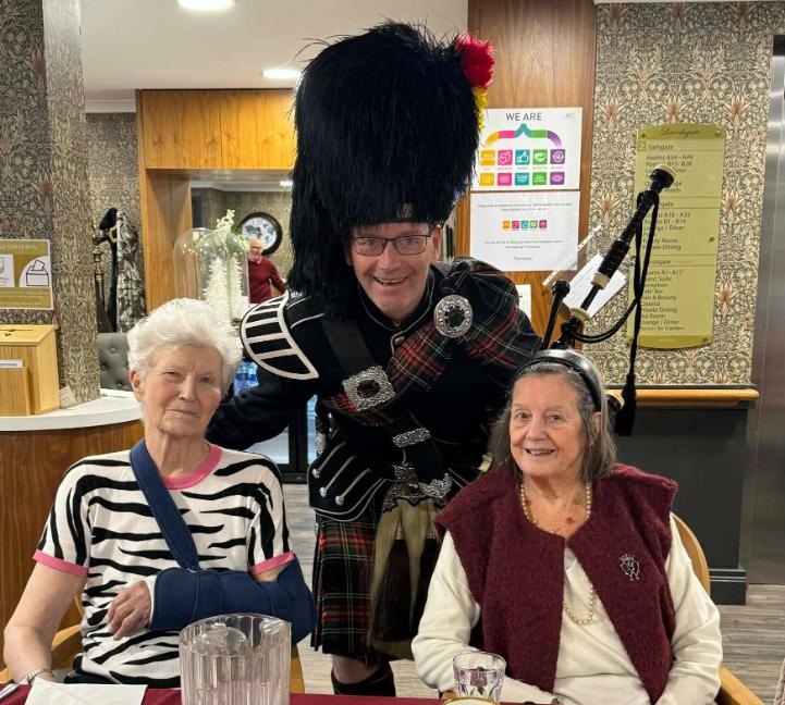 two older ladies sat down with a man in traditional scottish clothing