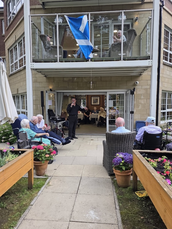 Man singing on garden patio for audience of elderly people